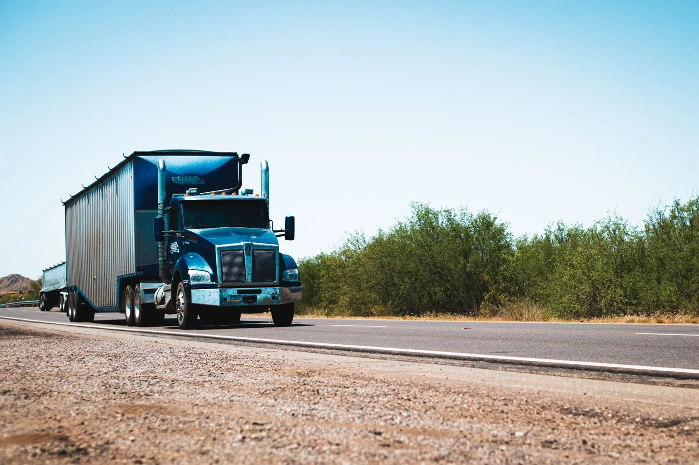 Blue American semi-truck traveling on a rural highway under clear skies